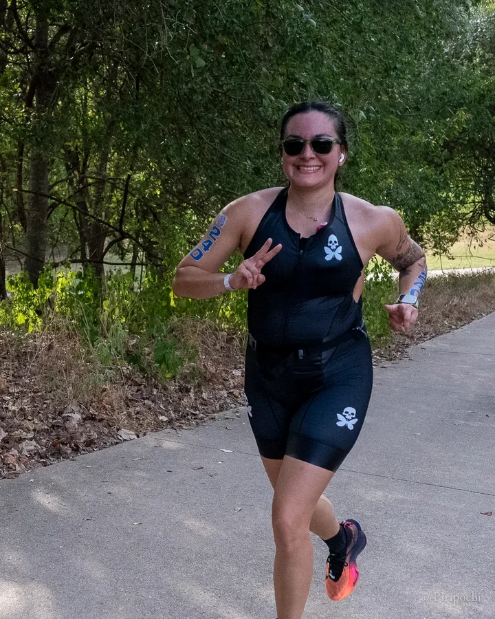 Atleta de triatlón corriendo sonriente y haciendo la señal de paz en un sendero entre árboles