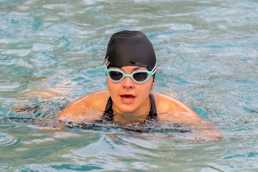 Atleta de triatlón nadando en una piscina, con gorro negro y gafas turquesa