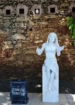 Tarjeta con una estatua viviente blanca frente a un muro de piedra